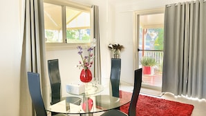 A dining area with a glass table, black chairs, a red vase with flowers, and a red rug. - Bright & Beautiful Home on the Hills! (Kelmscott)
