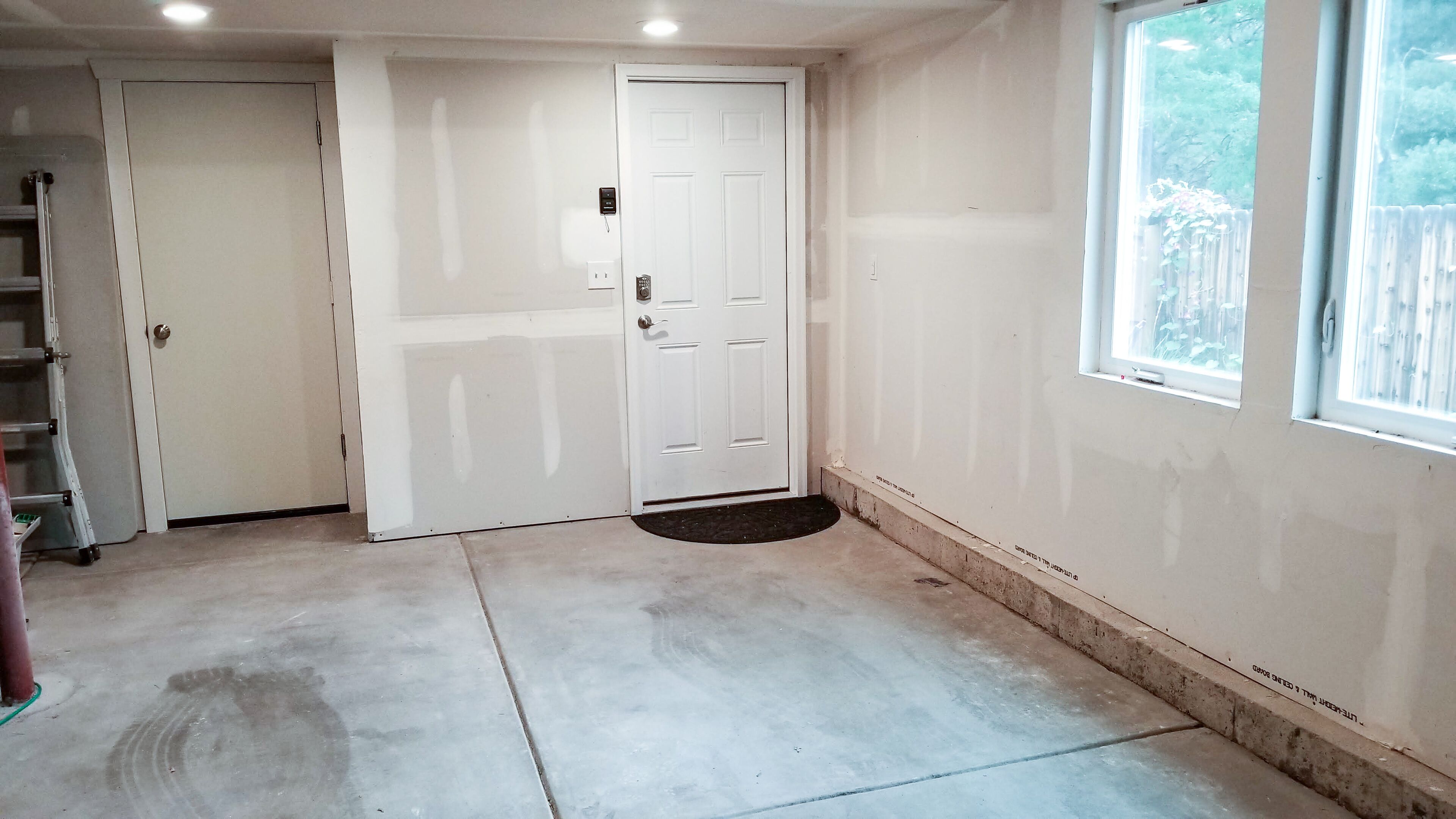 A room with a white door, a window, and a concrete floor.