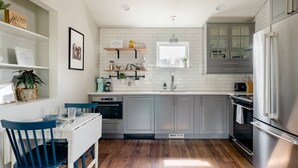 Una cocina moderna con armarios grises, un refrigerador de acero inoxidable, una mesa de comedor de madera con sillas azules y una ventana sobre el fregadero.