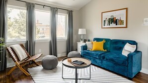 Una sala de estar moderna con un sofá azul, una silla de madera, una mesa de centro redonda y una alfombra a rayas.