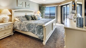 A bedroom with a bed, nightstand, lamp, and a view of the outdoors through a sliding glass door. - Land's End 403 building 9 Updated, beach front, close to pool|beach access (Treasure Island)
