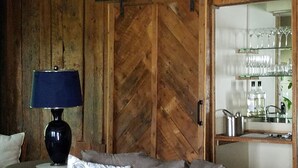 A room with a wooden herringbone floor, a sofa with floral cushions, a table with a lamp, and a glass cabinet with bottles and glasses. - Swim, Kayak,  lawn games. Walk to ice cream. Live Theatre , firepit smores!  (Harrison)