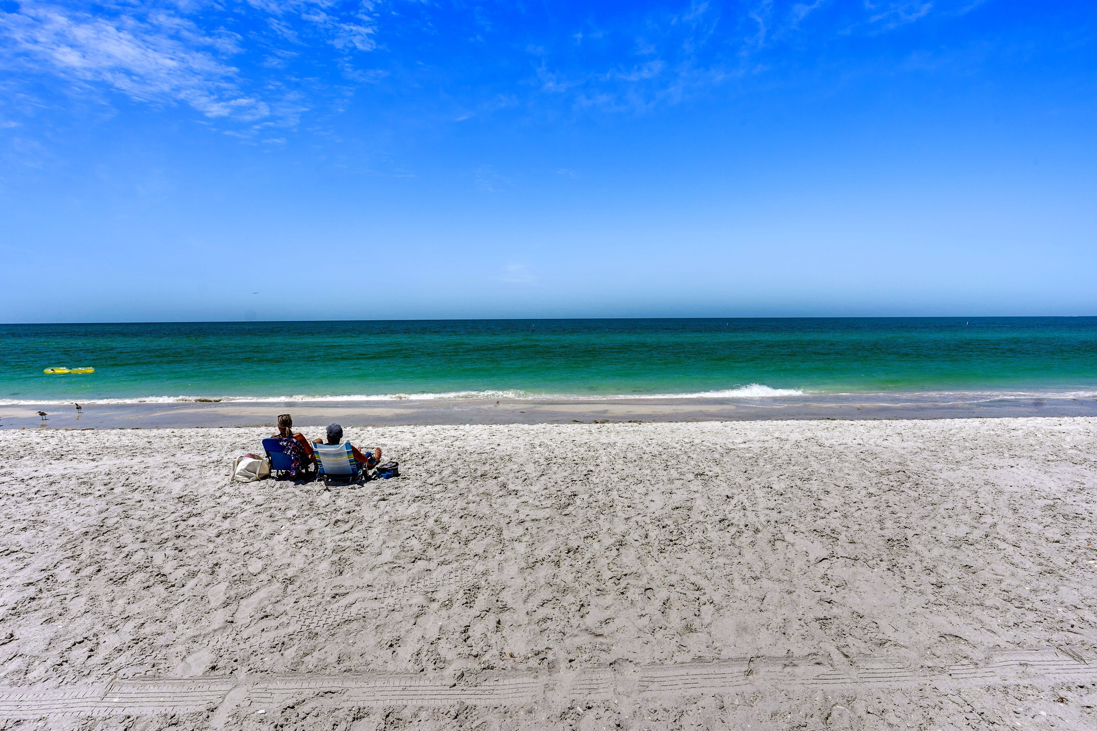 A beach with two people sitting on chairs facing the ocean.