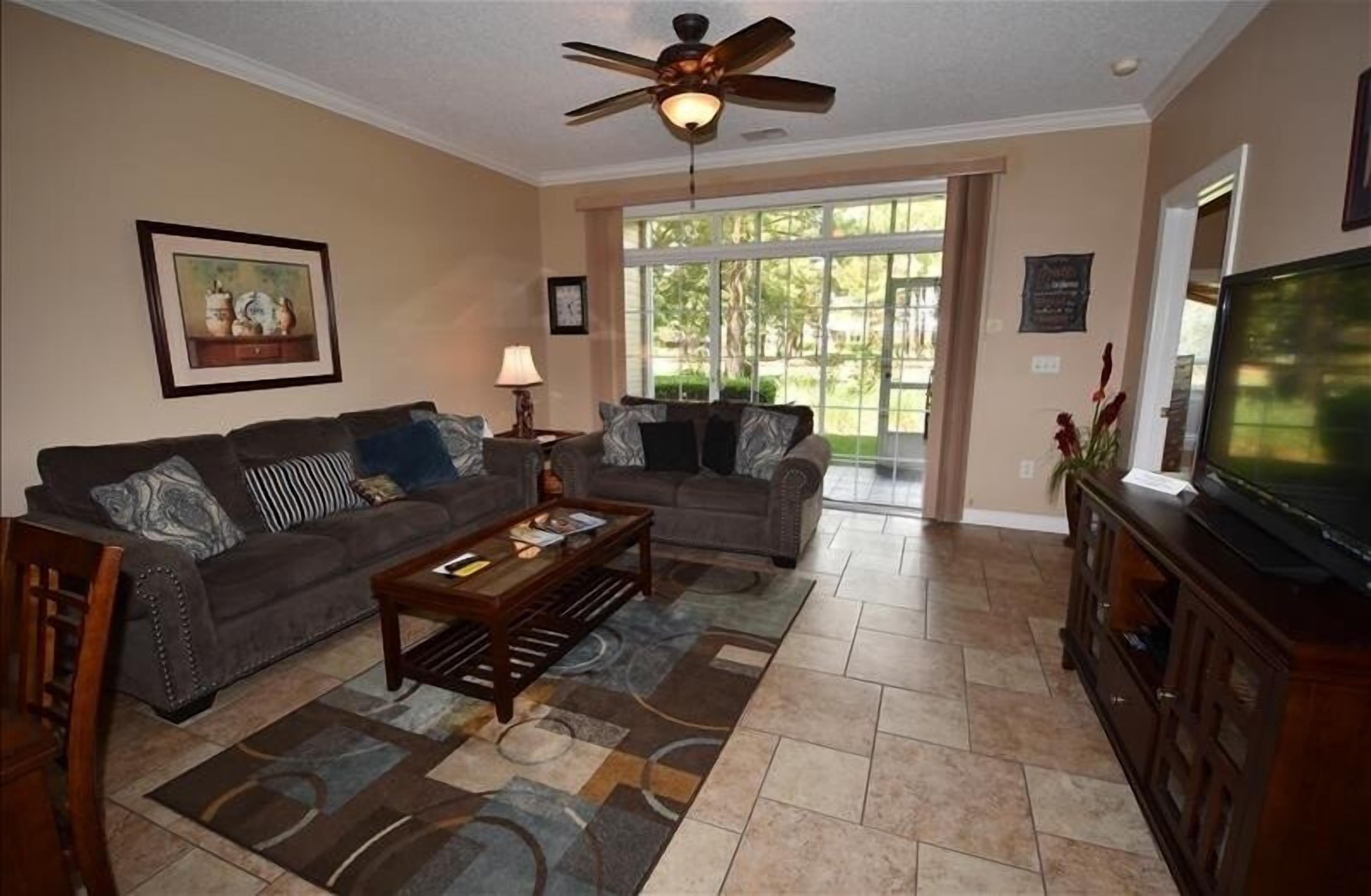 A living room with two sofas, a coffee table, a TV stand, and a ceiling fan.