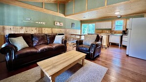 Un vaste espace de vie comprenant un canapé en cuir, une table basse en bois et une cuisine à l’arrière-plan.