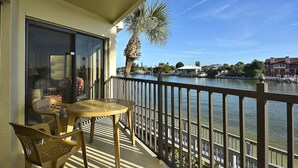 A balcony with a table and chairs, overlooking a body of water with a palm tree and buildings in the background. - Land's End 202 bldg 3~ Waterfront Views~ AMENITIES! (Treasure Island)