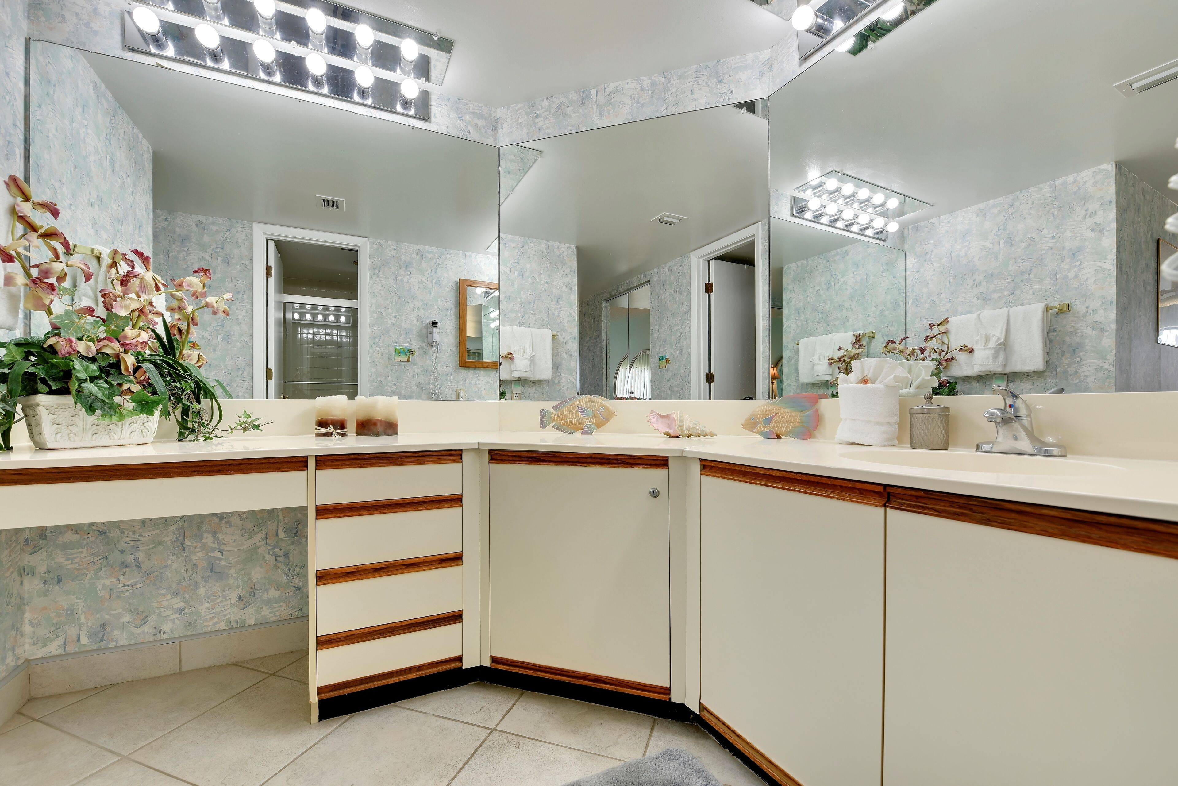 A modern bathroom with a large mirror, white vanity, and a floral arrangement.