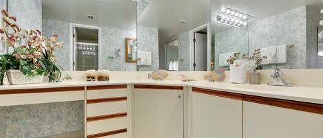 A modern bathroom with a large mirror, white vanity, and a floral arrangement.