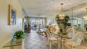 A dining area with wicker chairs, a glass table, and a chandelier. - Land's End 202 bldg 3~ Waterfront Views~ AMENITIES! (Treasure Island)