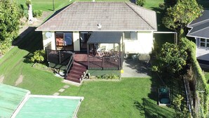 A house with a porch, a lawn, and a view of the water. - The Yellow Bach 90m to Campbells Beach; kayaks, wifi, Sky, Netflix, sleeps 4 (Campbells Beach)