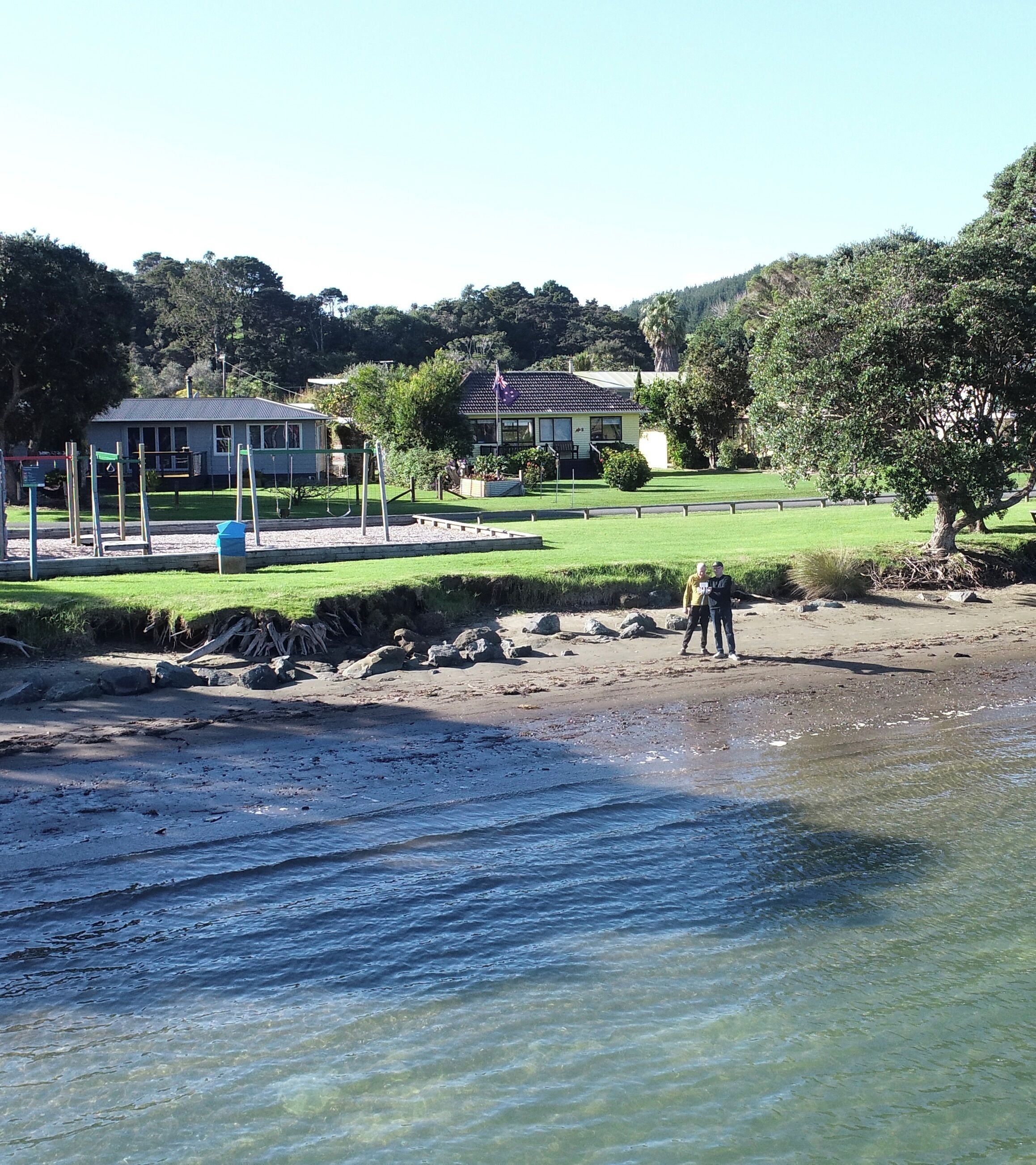 A beach with clear water, a playground, and houses in the background.