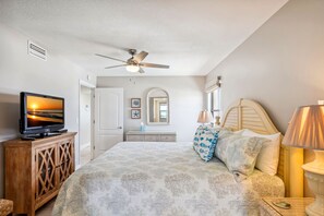 Cozy retreat with a large bed, ceiling fan, and TV, plus a bedside table and mirror.