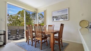 Un coin repas avec une table et des chaises en bois, une grande fenêtre donnant sur les arbres et un tableau encadré au mur.
