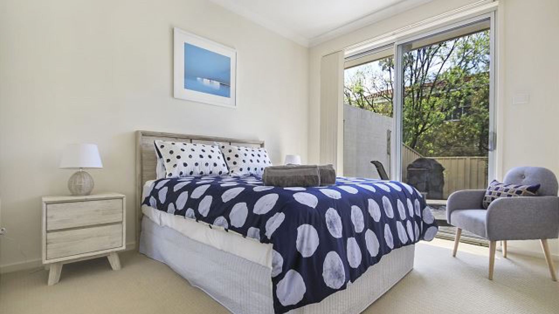 Un dormitorio con cama, una silla, una mesita de noche y una ventana.