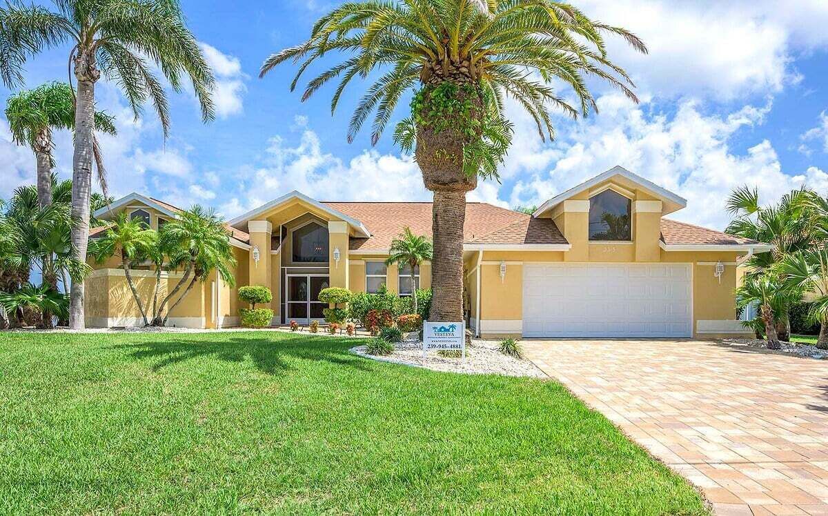 A two-story house with a garage, surrounded by palm trees and a well-maintained lawn.