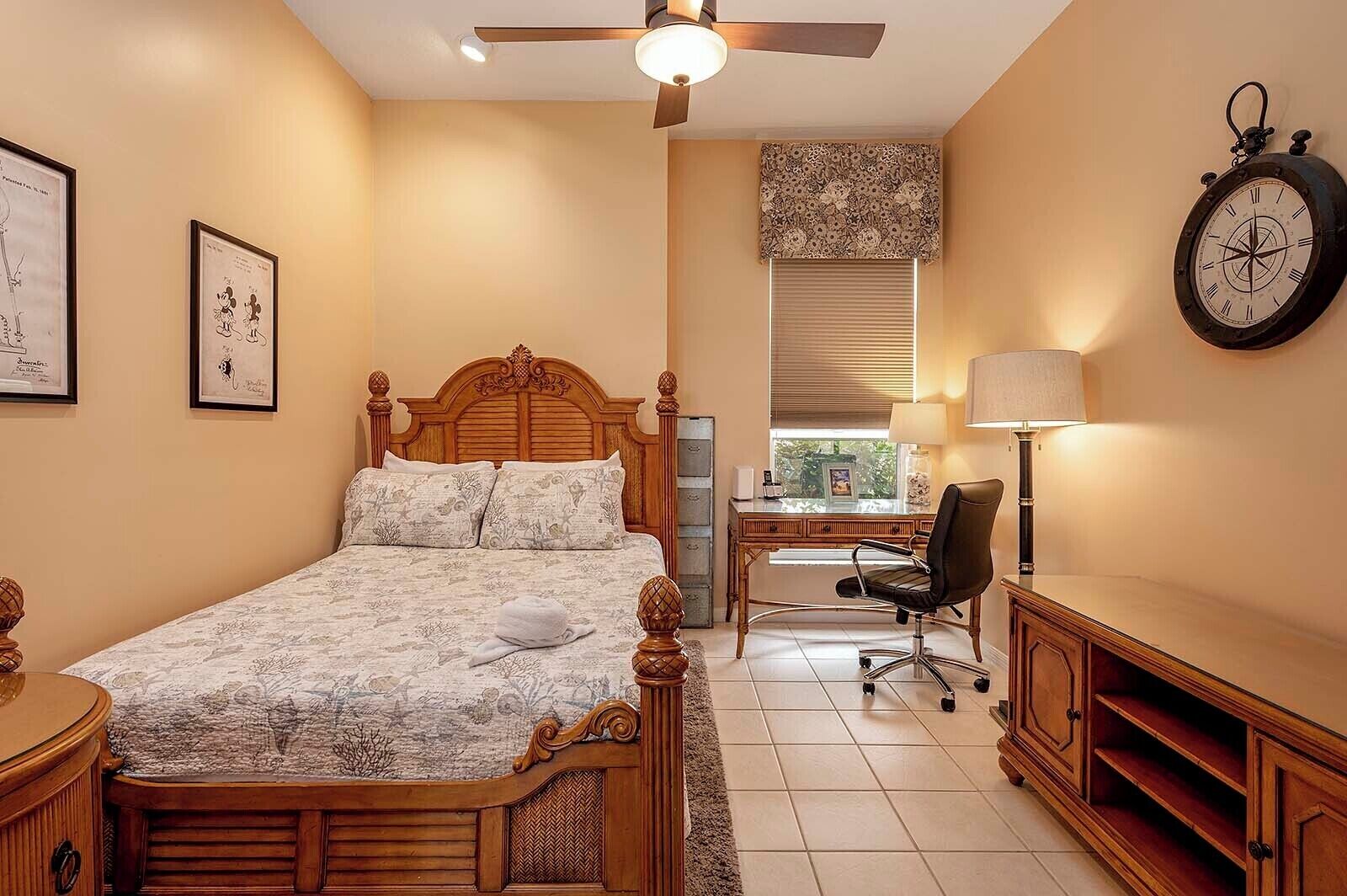 Een slaapkamer met een houten bed, een bureau, een stoel, een klok en wanddecoraties.