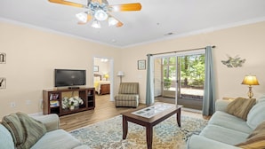 A living room with a television, a coffee table, and a sofa. There is a chair and a lamp in the room. - 314 Willow Bend - Barefoot Resort Rentals (North Myrtle Beach)