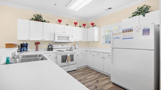 A modern kitchen with white cabinetry, a microwave, stove, and refrigerator. There are plants on the upper cabinets and a window with blinds. - 314 Willow Bend - Barefoot Resort Rentals (North Myrtle Beach)