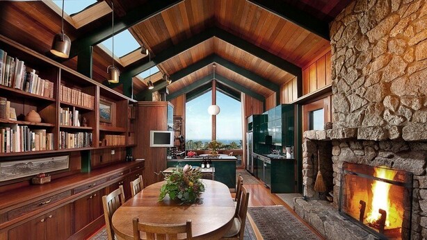 A spacious living area with a stone fireplace, wooden bookshelves, and a dining table with chairs. - Stunning Ranch Home with Ocean Views (Carmel)
