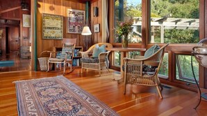 A cozy room with wooden floors, wicker furniture, and large windows offering a view of the outdoors. - Stunning Ranch Home with Ocean Views (Carmel)