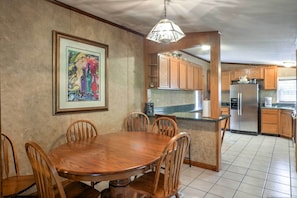 A dining area with a wooden table and chairs, a kitchen with wooden cabinets, and a hanging light fixture.