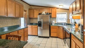 A compact kitchen with wooden cabinets, a stainless steel refrigerator, a built-in oven, and a window with blinds. - Ooltewah Cabin w/ Grill, Pool Table & Porch! (Ooltewah)