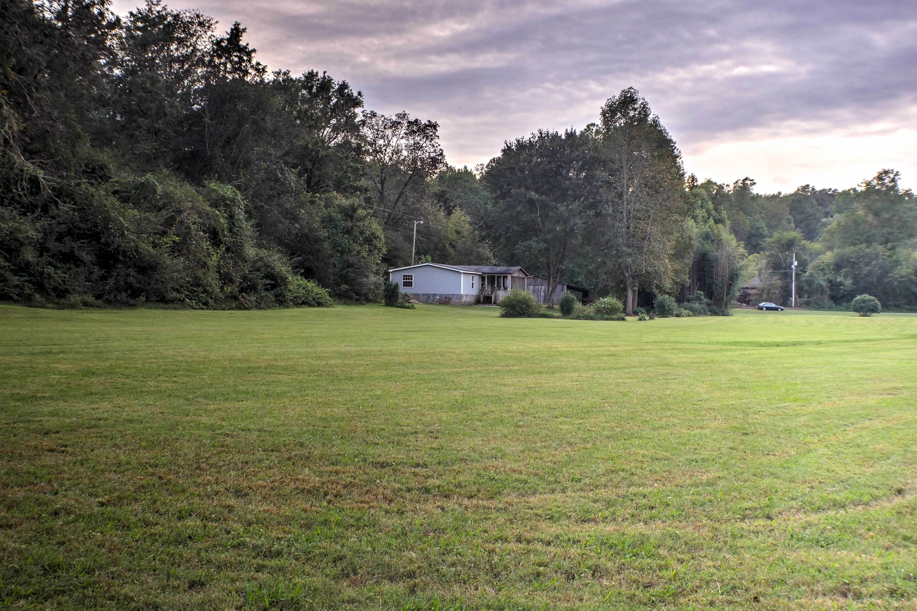 A grassy field with a small white building surrounded by trees.