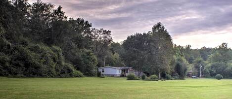 A grassy field with a small white building surrounded by trees.