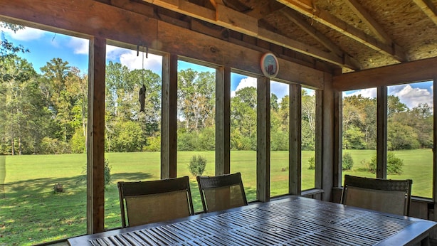 A wooden-paneled room with a large table and chairs, large windows offering a view of a green lawn and trees. - Ooltewah Cabin w/ Grill, Pool Table & Porch! (Ooltewah)