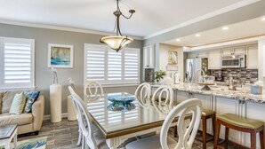 A modern kitchen with white cabinetry, a central island, and a dining area with a glass-top table and white chairs.