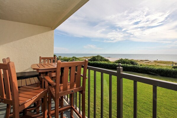 Ein Balkon mit Holzmöbeln mit Blick auf Strand und Meer.