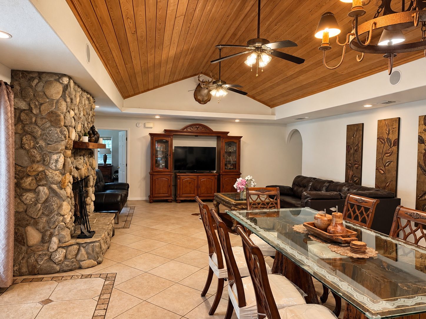 A spacious living area with a stone wall, a fireplace, a television, and a dining table with chairs.