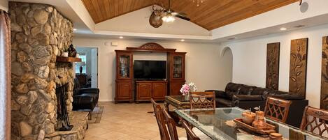 A spacious living area with a stone wall, a fireplace, a television, and a dining table with chairs.
