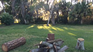 A fire pit with logs and a stone fire ring in a grassy outdoor area. - Beautiful Vacation Home Across from Lake Okeechobee (Okeechobee)