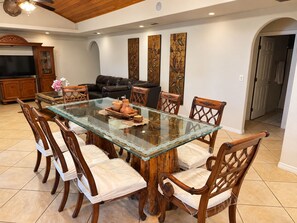 A dining area with a glass-top table surrounded by wooden chairs with cushioned seats, a black leather sofa, and a wooden cabinet with a television. - Beautiful Vacation Home Across from Lake Okeechobee (Okeechobee)