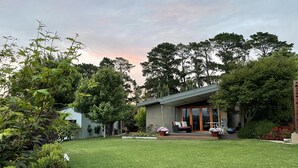 Une maison moderne dotée d’un vaste jardin, d’une terrasse avec mobilier d’extérieur et d’une grande variété de plantes et de fleurs.
