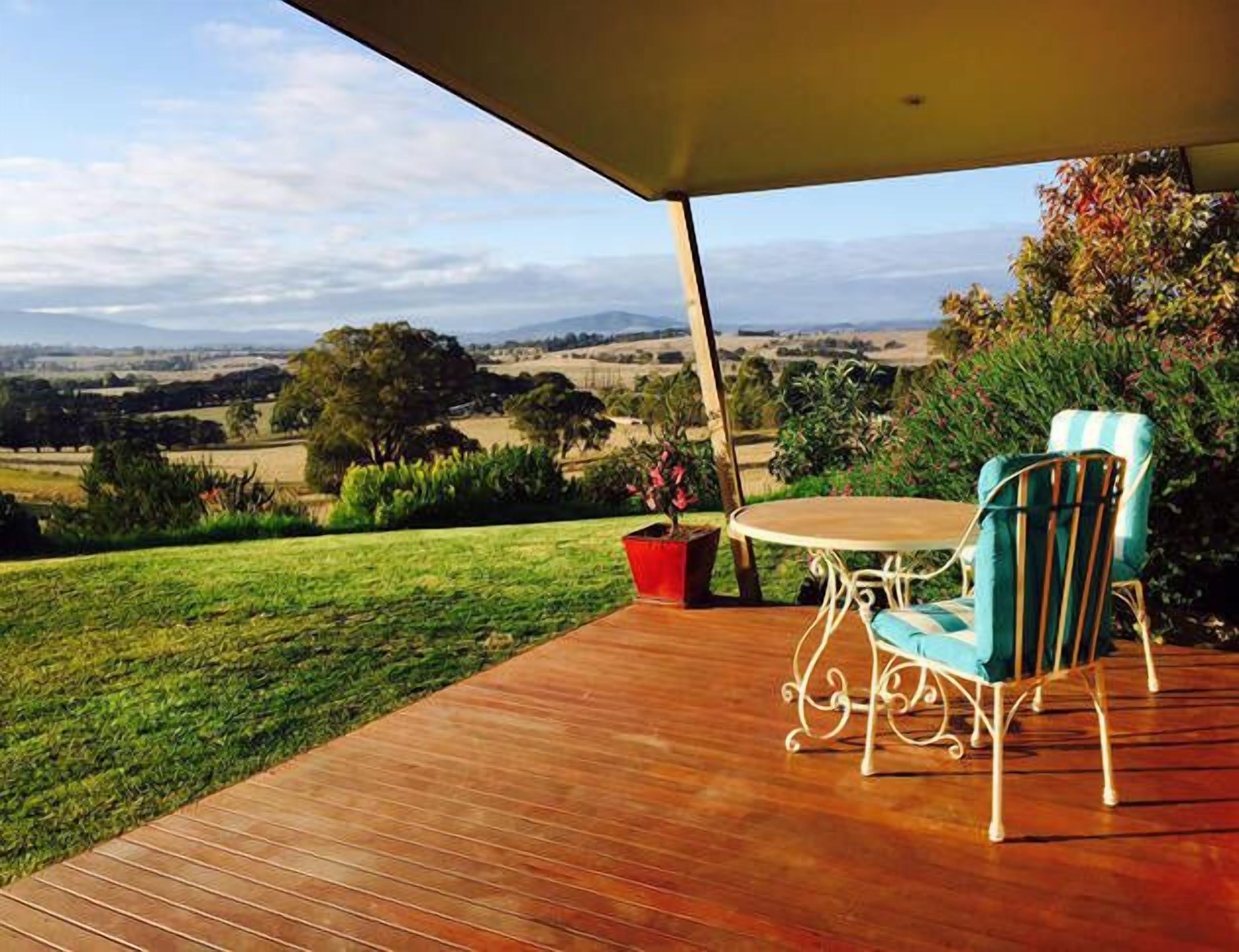 An outdoor patio with a wooden deck, a round table, and two chairs with striped cushions.