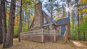 A cabin with a stone chimney, wooden deck, and a green door. - Secluded Conway Home w/ Theater Room & Hot Tub! (Conway)