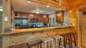 A kitchen with wooden cabinets, stainless steel appliances, and a bar area with stools. - Secluded Conway Home w/ Theater Room & Hot Tub! (Conway)
