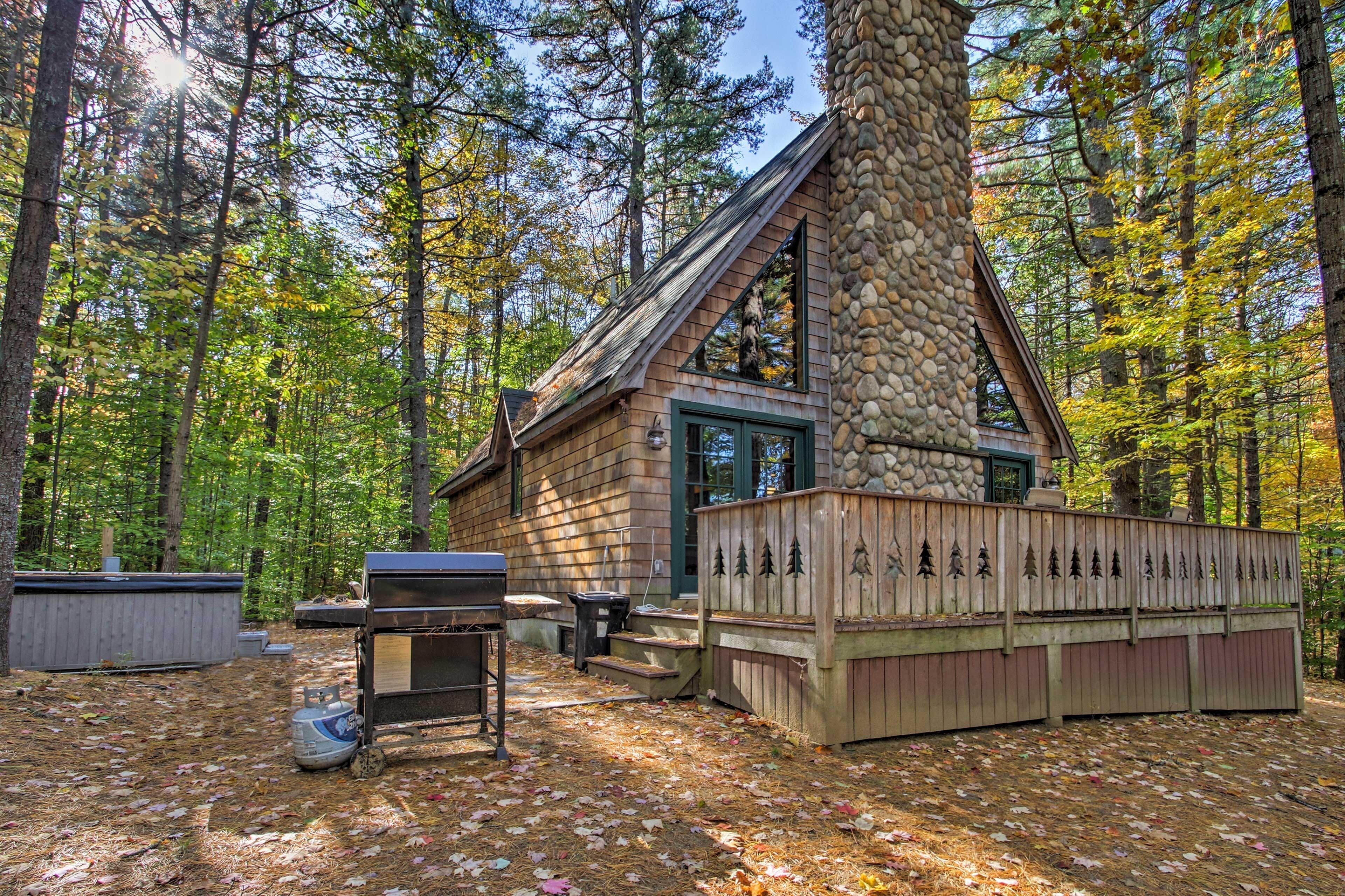 A cabin with a stone chimney, surrounded by a wooden deck and a forest.