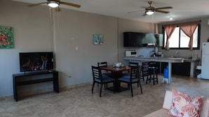A living room with a TV, dining table, chairs, ceiling fans, and a kitchen area with cabinets and appliances. - Affordable Furnished 2-Story Ocean view Townhouse (San Jacinto)