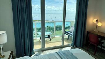 Habitación de hotel con ventana grande, cama, escritorio, silla y mesa con vistas al mar y barcos.