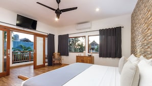 Hotelkamer met een bed, bureau, stoel, televisie en balkon met uitzicht op groen.