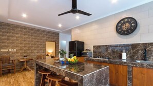 Een moderne keuken met een marmeren eiland, houten barstoelen, een ingebouwde magnetron en een grote decoratieve klok aan de muur.