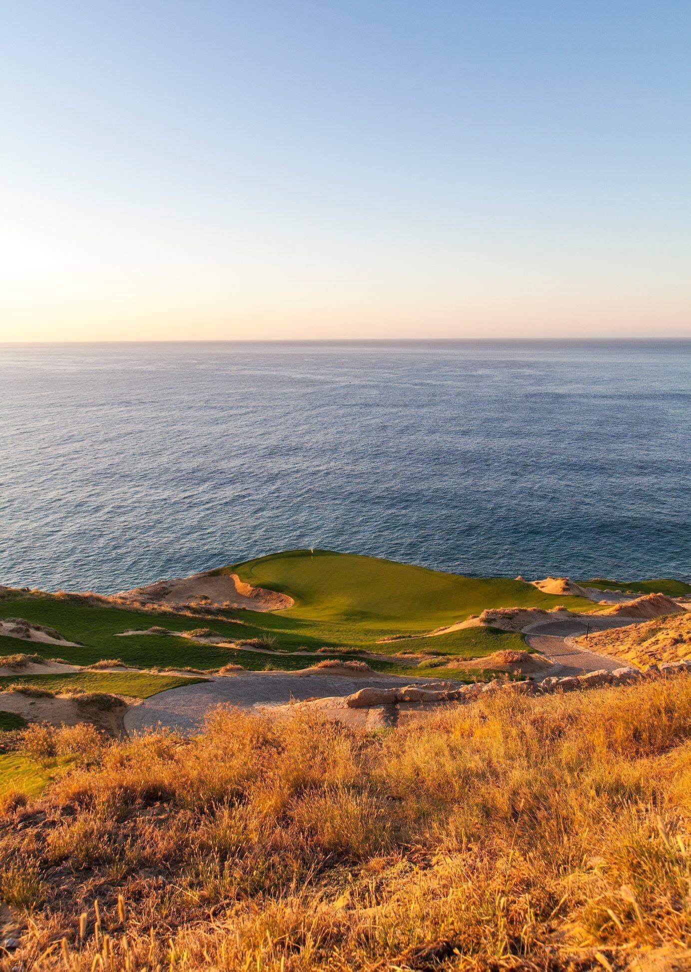 En kystgolfbane med kig til havet, sandet terræn og grønne fairways.