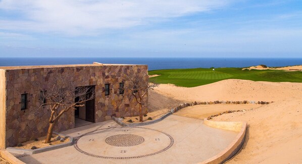 Un edificio moderno con fachada de piedra, un patio circular y vistas al océano y a un campo de golf.