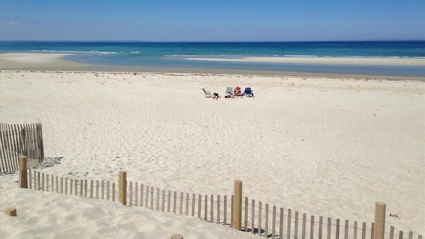 Une plage avec une clôture en bois et quelques personnes assises sur le sable.