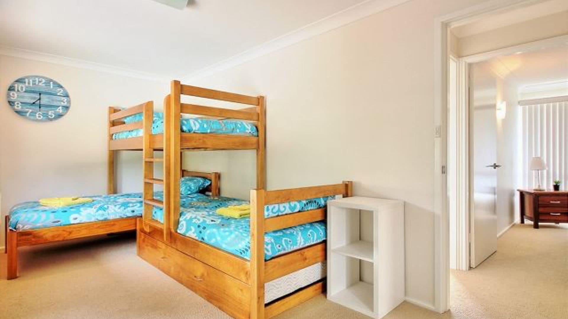A bedroom with two bunk beds, a wall clock, and a small desk with a lamp.