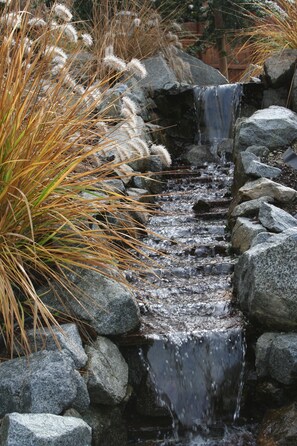 Une petite cascade d’eau qui dévale sur des rochers, dans un cadre de jardin.