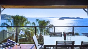 Un comedor con mesa y sillas, con vistas panorámicas al mar y las colinas.